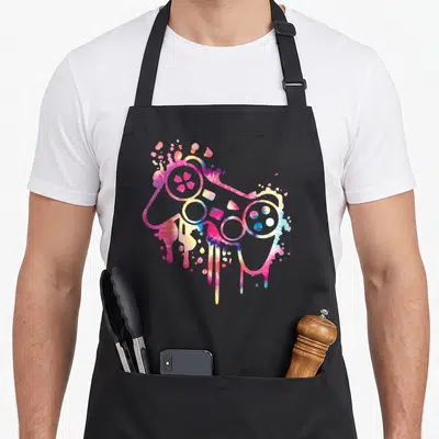 Tablier de cuisine noir avec une manette de jeu vidéo tie dye aux couleurs vives et effet de peinture qui dégouline.