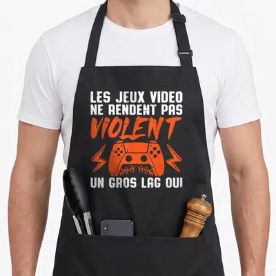 Tablier de cuisine noir avec une console orange, des éclairs et le texte Les jeux vidéo ne rendent pas violent un gros lag oui.