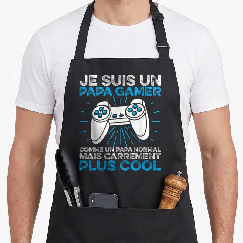 Tablier de cuisine noir avec illustration de manette et texte Je Suis Un Papa Gamer Plus Cool en blanc et bleu.