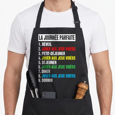 Tablier de cuisine noir avec programme La Journée Parfaite alternant repas et sessions de jeu vidéo en couleurs vives sur fond gris.