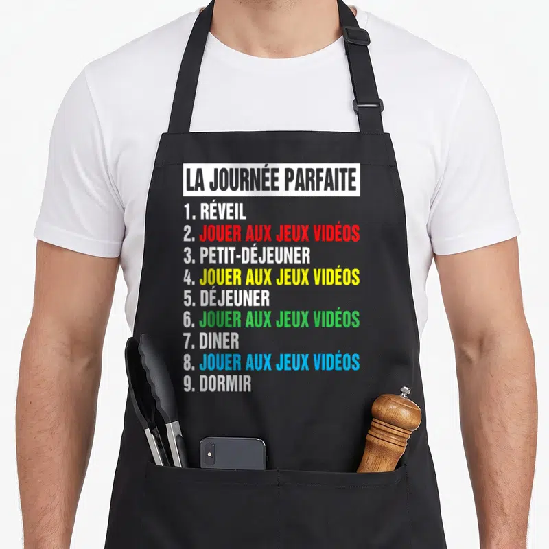 Tablier de cuisine noir avec programme La Journée Parfaite alternant repas et sessions de jeu vidéo en couleurs vives sur fond gris.