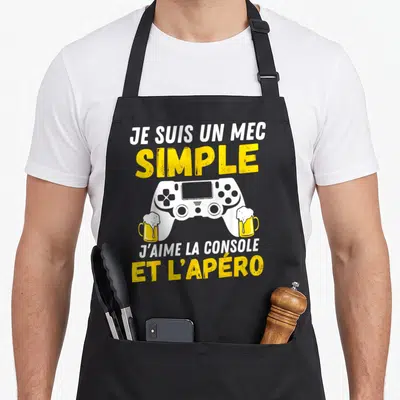 Tablier de cuisine noir avec une manette de jeu vidéo blanche tenant deux verres de bière et du texte humoristique en blanc et jaune.