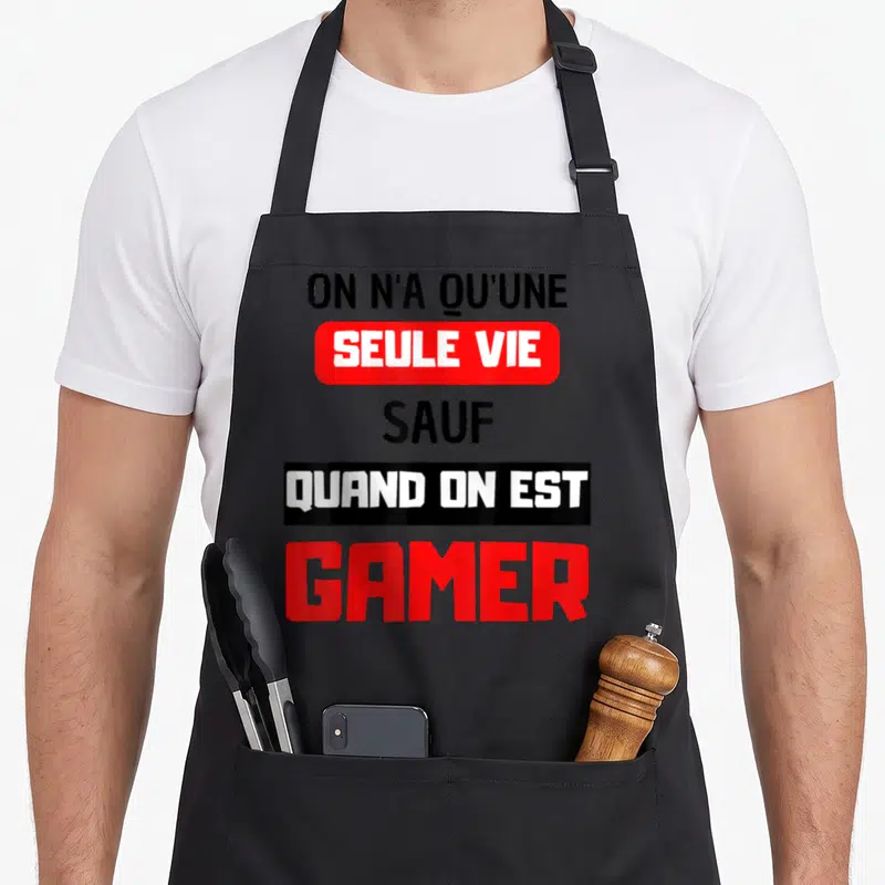 Tablier de cuisine noir avec le texte On n'a qu'une seule vie sauf quand on est gamer en rouge et blanc.