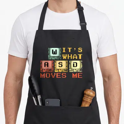 Tablier de cuisine noir avec les lettres W A S D colorées et le texte It's what moves me en pixel art.
