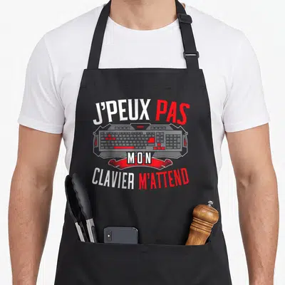 Tablier de cuisine noir avec illustration de clavier et texte J'peux pas mon clavier m'attend en blanc et rouge.
