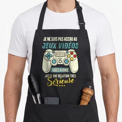 Tablier de cuisine noir avec illustration de manette de jeu et texte humoristique sur la relation sérieuse avec les jeux vidéos.