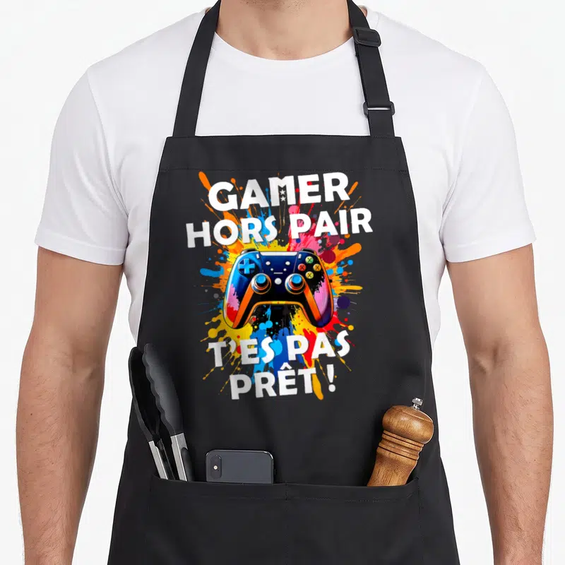Tablier de cuisine noir avec manette de jeu colorée et texte Gamer Hors Pair T'es Pas Prêt sur fond d'éclaboussures.
