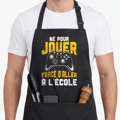 Tablier de cuisine noir avec une manette de jeu jaune et texte blanc sur fond uni.