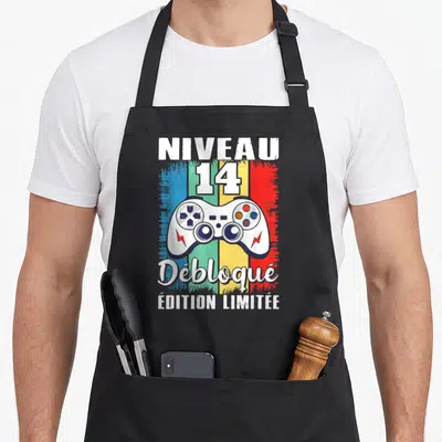 Tablier de cuisine noir orné d'une manette blanche sur fond coloré et du texte Niveau 14 Débloqué « Édition Limitée ».