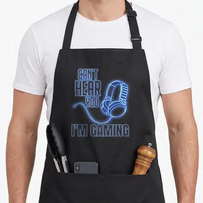 Tablier de cuisine noir avec inscription Je Ne Peux Pas T'Entendre Je Joue et illustration de casque audio bleu lumineux.