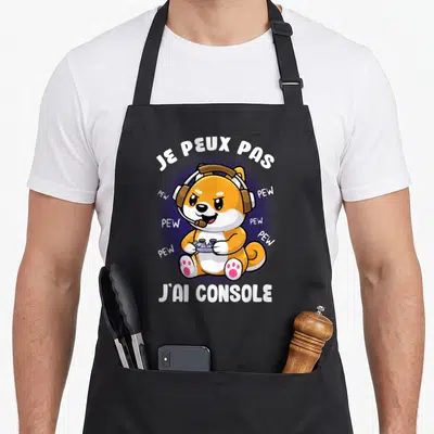 Tablier de cuisine noir avec illustration de chien orange portant un casque et tenant une manette de jeu vidéo.