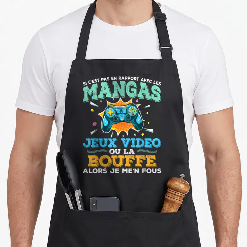 Tablier de cuisine noir avec une manette de jeu vidéo bleue et un slogan humoristique sur les mangas et la bouffe.