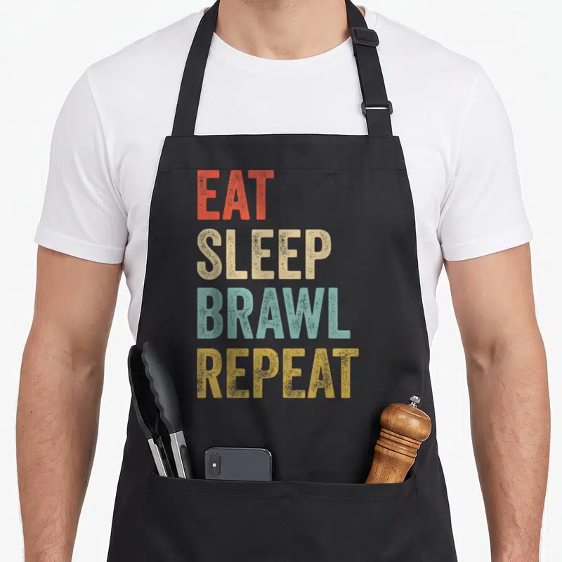Tablier de cuisine noir avec l'inscription Eat Sleep Brawl Repeat en lettres colorées et texturées.