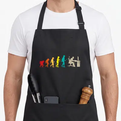 Tablier de cuisine noir avec une illustration colorée représentant l'évolution du gamer jusqu'au joueur devant son ordinateur.
