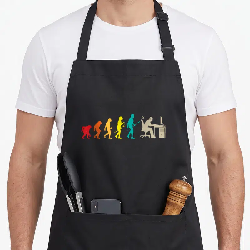 Tablier de cuisine noir avec une illustration colorée représentant l'évolution du gamer jusqu'au joueur devant son ordinateur.