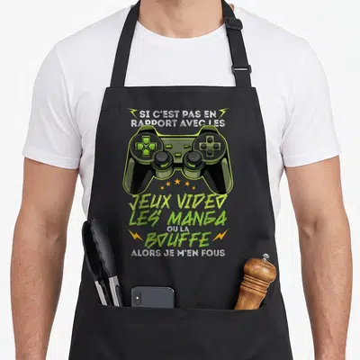 Tablier de cuisine noir avec illustration de manette de console verte et texte humoristique sur les jeux vidéo et les manga.