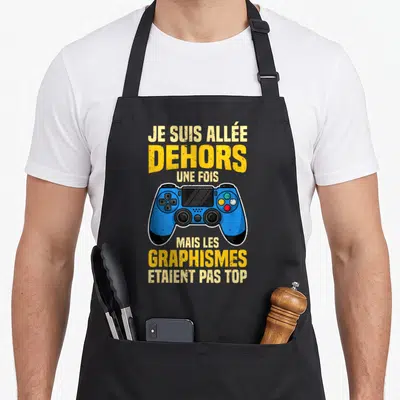 Tablier de cuisine noir avec une manette de jeu bleue et le texte Je suis allée dehors une fois mais les graphismes étaient pas top.