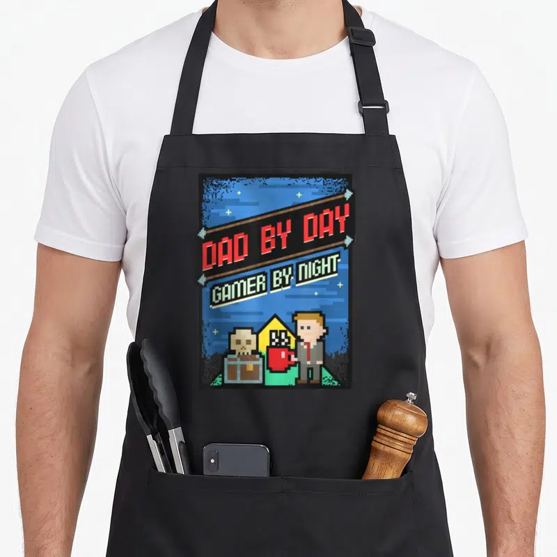Tablier de cuisine noir avec motif pixel art Dad by Day Gamer by Night et personnage en costume tenant une tasse rouge.