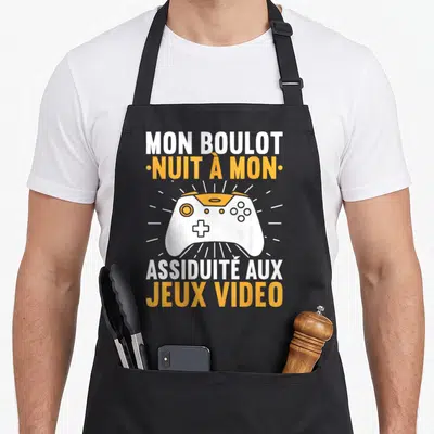 Tablier de cuisine noir avec une illustration de manette de jeu blanche et orange entourée de rayons lumineux.