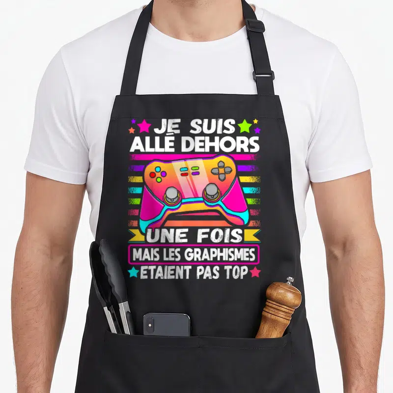 Tablier de cuisine noir avec manette colorée et texte humoristique sur le gaming.