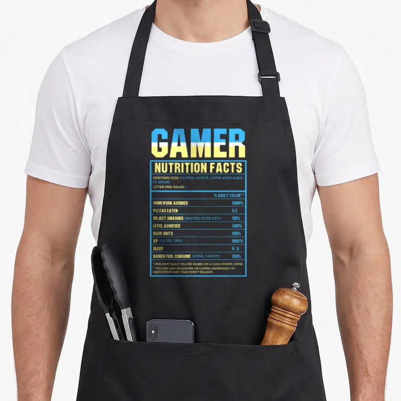 Tablier de cuisine noir avec une étiquette bleue et jaune Gamer Nutrition Facts imprimée au centre.