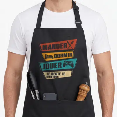 Tablier de cuisine noir avec bandes colorées Manger Dormir Jouer et une manette de jeu vidéo imprimée.