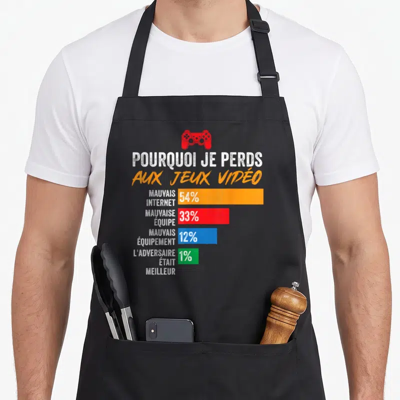 Tablier de cuisine noir avec un graphique humoristique sur les raisons de perdre aux jeux vidéo et une manette rouge.