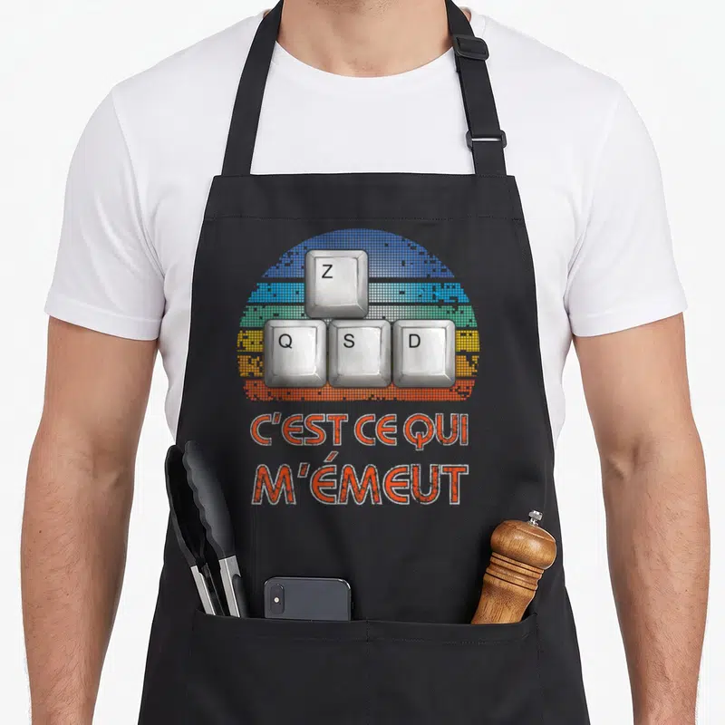 Tablier de cuisine noir avec illustration de touches ZQSD et texte orange C'est ce qui m'émeut sur fond rétro pixelisé.