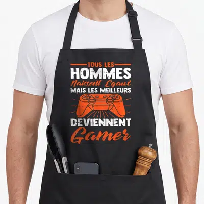Tablier de cuisine noir avec texte blanc et orange et illustration de manette de jeu vidéo au centre du motif imprimé.