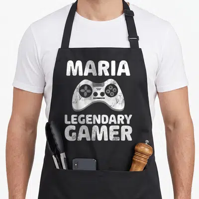 Tablier de cuisine noir avec le nom Maria, une manette de jeu et le texte Legendary Gamer en blanc texturé.