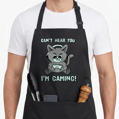 Tablier de cuisine noir avec illustration d'un chat gris portant un casque et tenant une manette de jeu vidéo.