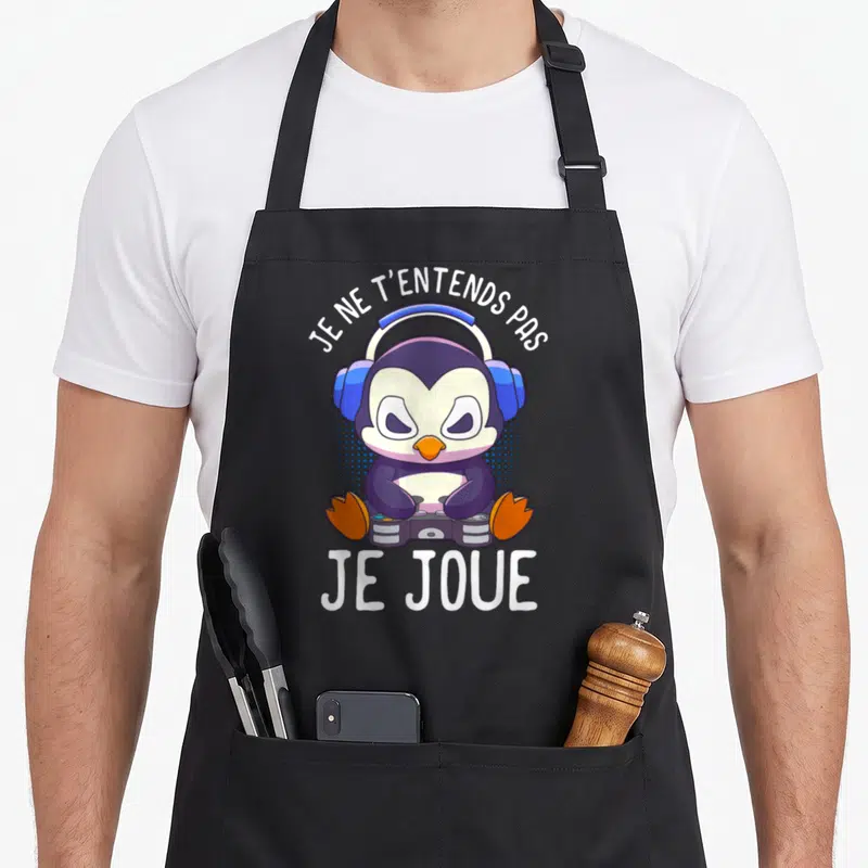 Tablier de cuisine noir avec manchot violet casqué tenant une manette et le texte Je ne t'entends pas je joue