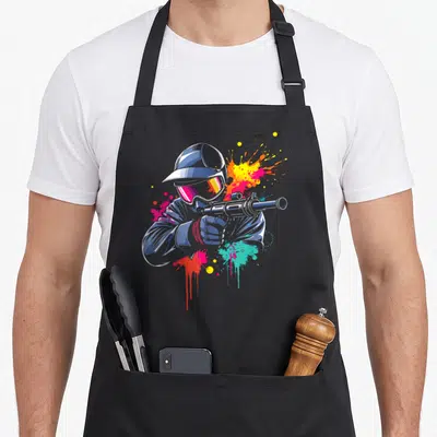 Tablier de cuisine noir avec illustration d'un joueur de paintball visant et des éclaboussures de peinture colorées.