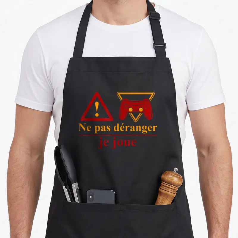 Tablier de cuisine noir avec une manette rouge et l'inscription Ne pas déranger je joue en orange et rouge.