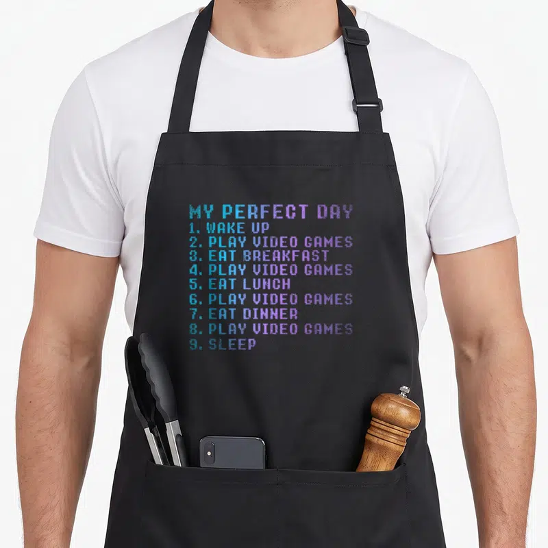 Tablier de cuisine noir avec une liste textuelle colorée My Perfect Day et Play Video Games en style pixel art.