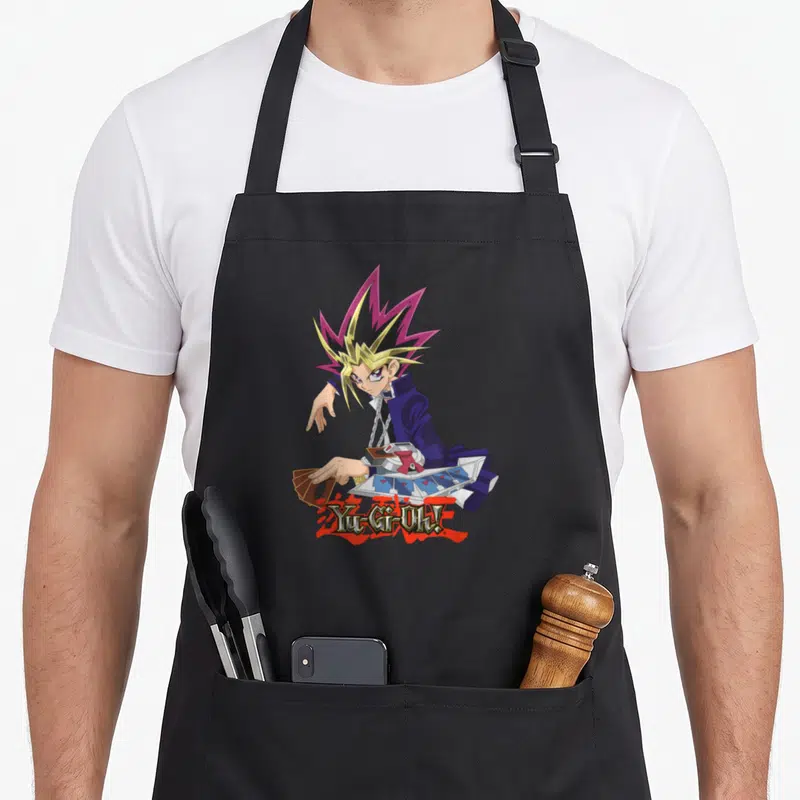 Tablier de cuisine noir avec illustration de Yugi jouant aux cartes et le logo Yu-Gi-Oh.