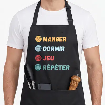 Tablier de cuisine noir avec les mots Manger Dormir Jeu Répéter accompagnés d'icônes colorées verticales.