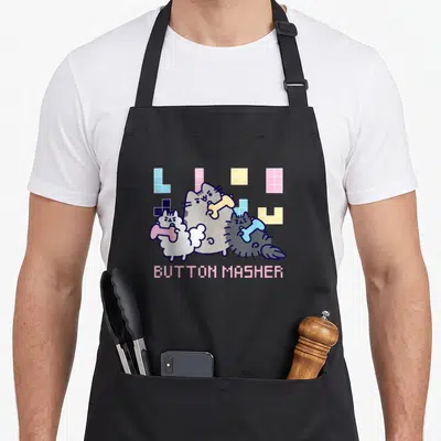 Tablier de cuisine noir avec trois chats tenant des os et l'inscription Button Masher en lettres roses pixelisées.