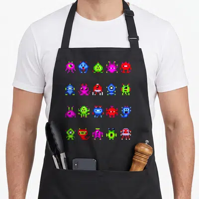 Tablier de cuisine noir avec une grille de petits monstres pixelisés multicolores dans un style art rétro gaming.