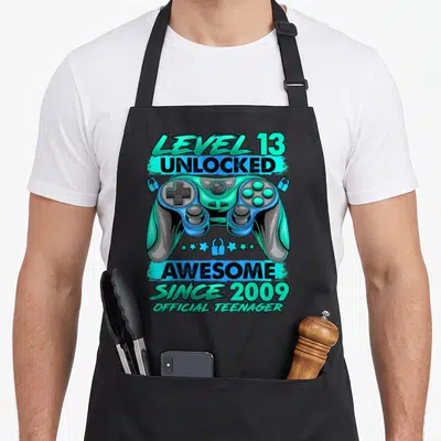 Tablier de cuisine noir avec illustration de manette bleue et texte Level 13 Débloqué Génial Depuis 2009 Official Teenager.