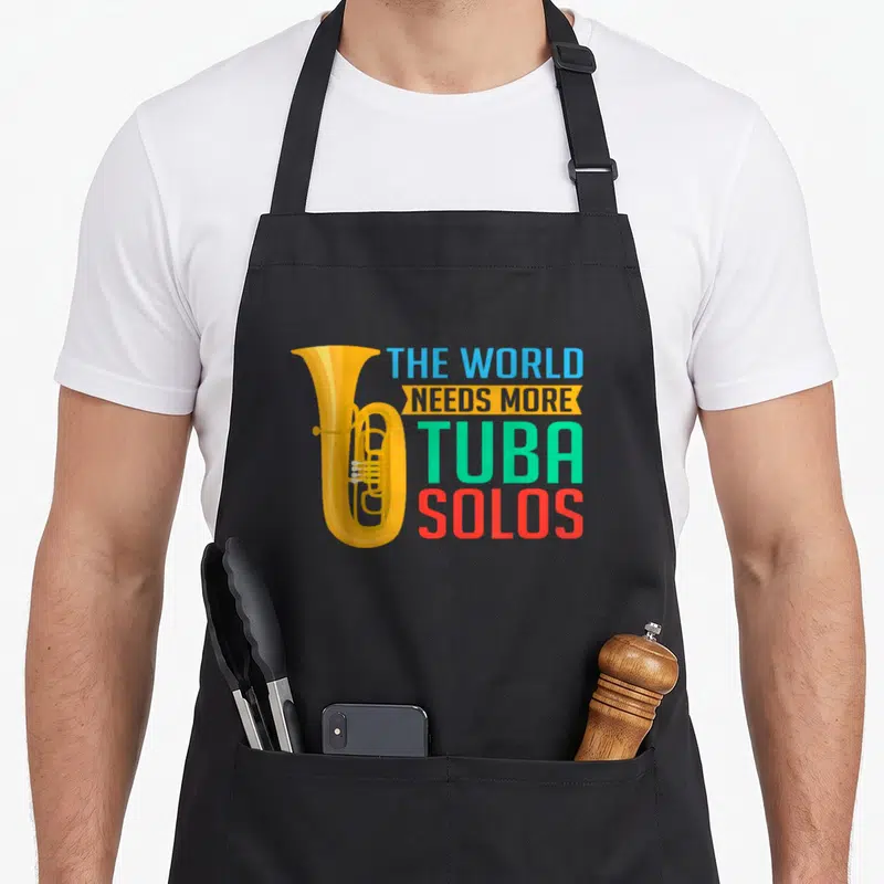 Tablier de cuisine noir avec illustration de tuba jaune et texte THE WORLD NEEDS MORE TUBA SOLOS multicolore