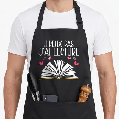 Tablier de cuisine noir avec inscription J'peux pas j'ai lecture et illustration de livre ouvert entouré de cœurs roses.