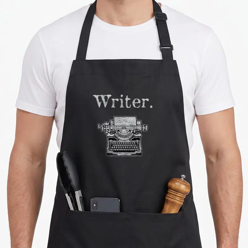 Tablier de cuisine noir avec l'inscription Writer. au-dessus d'un dessin détaillé de machine à écrire vintage en noir et blanc.