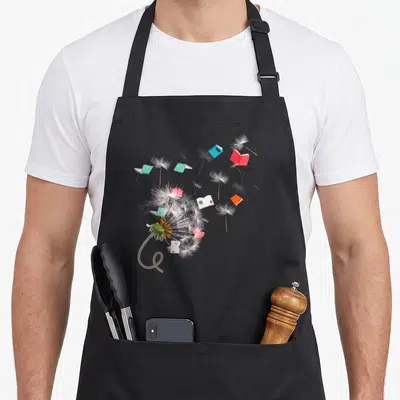 Tablier de cuisine noir avec un pissenlit dont les graines deviennent des livres ouverts aux couleurs vives.