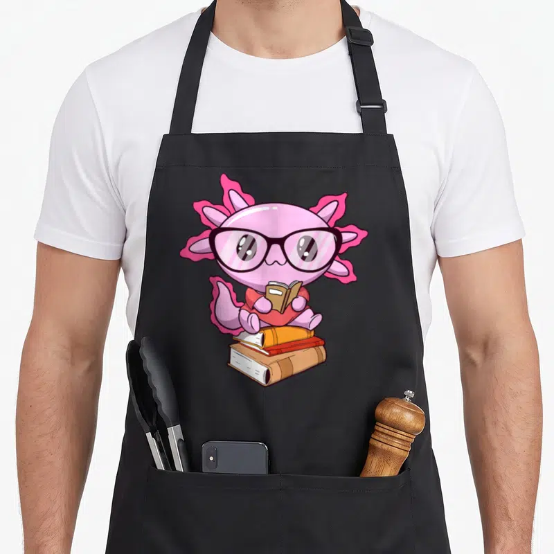 Tablier de cuisine noir avec illustration d'un axolotl rose aux lunettes lisant un livre posé sur des ouvrages empilés.