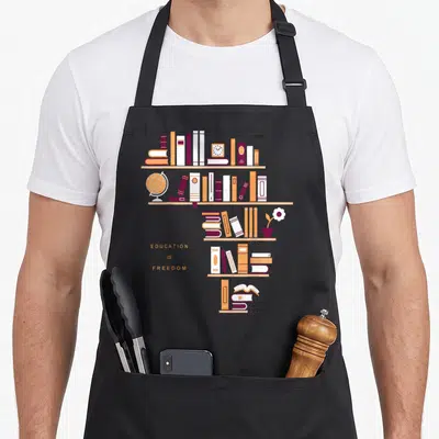 Tablier de cuisine noir avec illustration d'étagères de livres, un globe terrestre et le texte Education Is Freedom en orange.