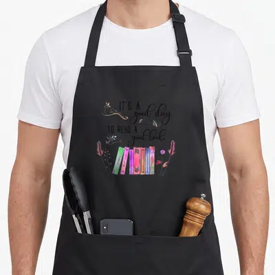 Tablier de cuisine noir avec inscription It's a good day to read a good book et illustrations de livres colorés.