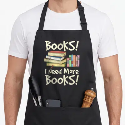 Tablier de cuisine noir avec illustration de livres empilés et texte Books I Need More Books en lettres crème.