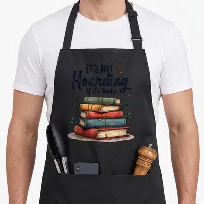 Tablier de cuisine noir avec une illustration de cinq livres empilés et le texte It's Not Hoarding if it's books entouré d'étoiles dorées.