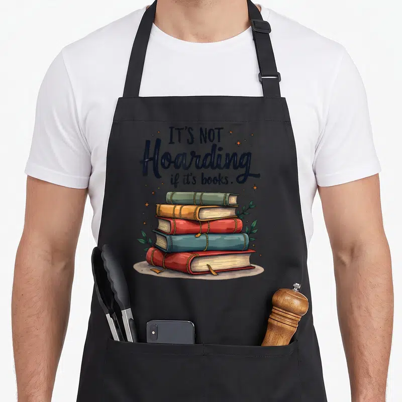 Tablier de cuisine noir avec une illustration de cinq livres empilés et le texte It's Not Hoarding if it's books entouré d'étoiles dorées.